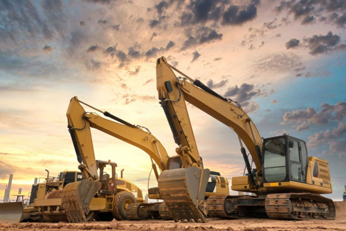 Two yellow excavators parked next to other heavy machinery outside
